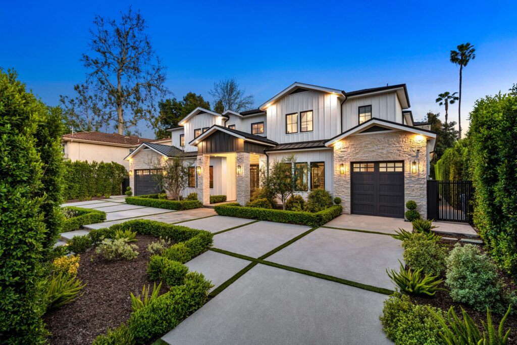 Modern two-story house with large windows, double garages, and manicured landscaping, featuring concrete walkways, lush greenery, and exterior lights at dusk under a clear blue sky. An example of a non-countable asset if used as a primary residence.